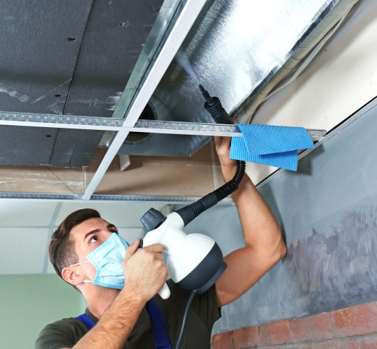 Male technician cleaning industrial air conditioner indoors