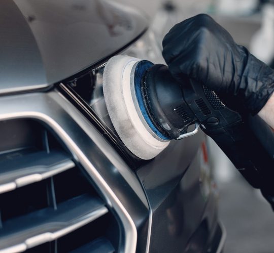 Man in a garage. Worker polish a car.